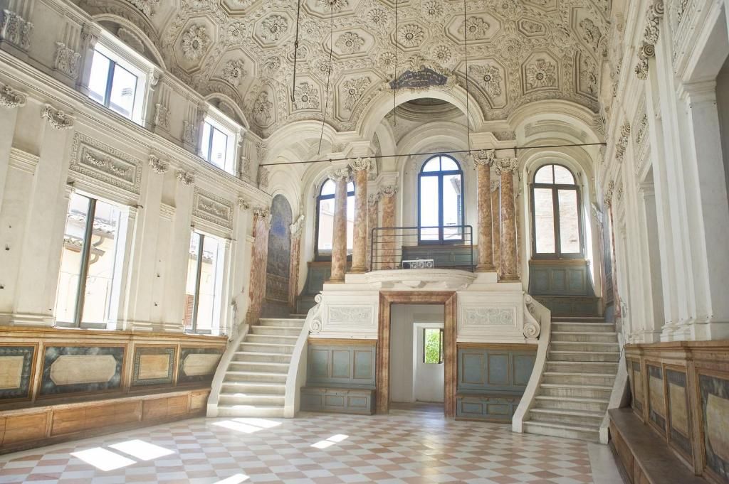 Un interior ornamentado con una imponente escalera, ventanas arqueadas y un suelo a cuadros.