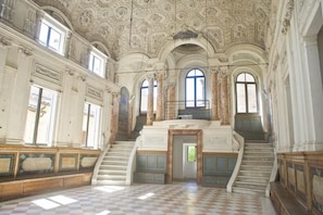 An ornate interior with a grand staircase, arched windows, and a checkered floor. - Maison Mare&Monti (Pesaro)