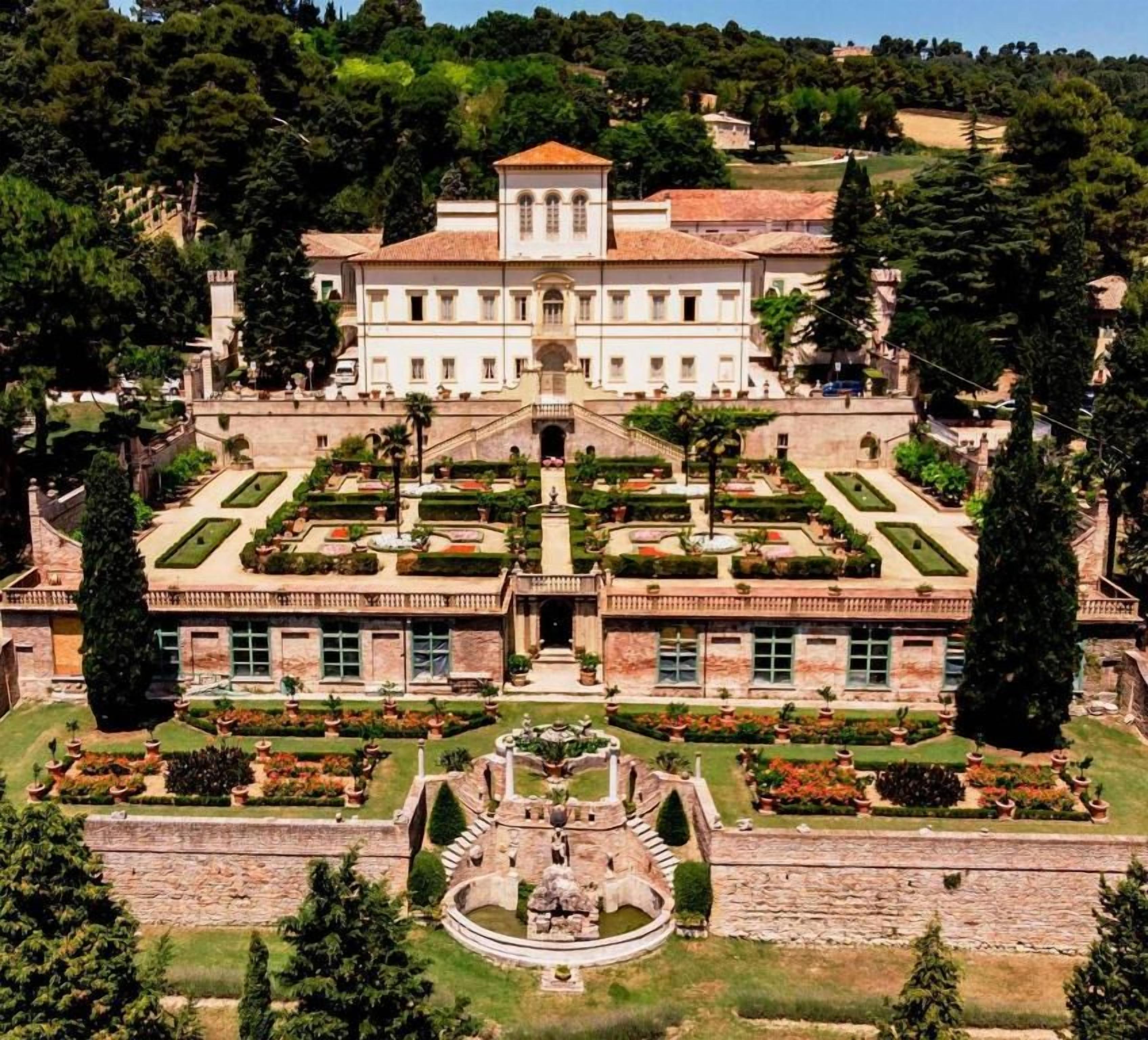 Un grand bâtiment historique à la façade symétrique, doté d’une cour intérieure avec une fontaine et d’un jardin aménagé dans un style formel.