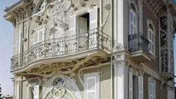 Un edificio de dos pisos con detalles arquitectónicos ornamentales, un balcón y un césped bien cuidado.