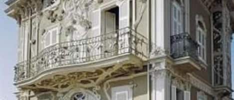 Un edificio de dos pisos con detalles arquitectónicos ornamentales, un balcón y un césped bien cuidado.