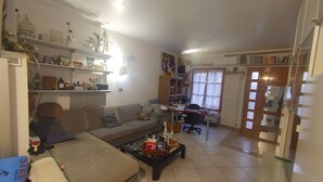 A living room with a sofa, coffee table, and a desk with a computer. There are shelves with various items and a window with blinds. - Maison Mare&Monti (Pesaro)
