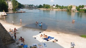 En strand ved en flod, hvor folk bader og soler sig.
