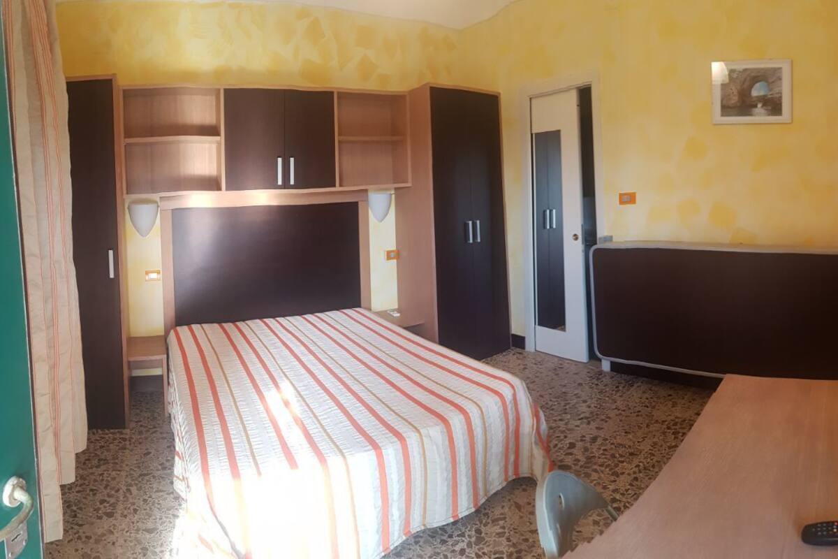 A hotel room with a bed, a desk, a chair, a TV, and a wardrobe.