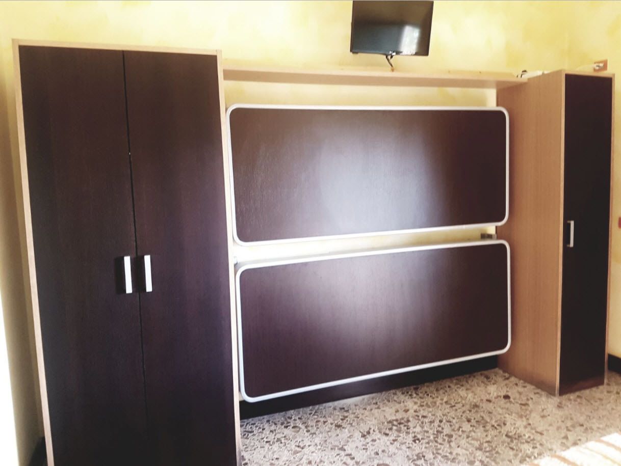 A room with a dark brown wardrobe, a double door, and a television mounted on the wall.