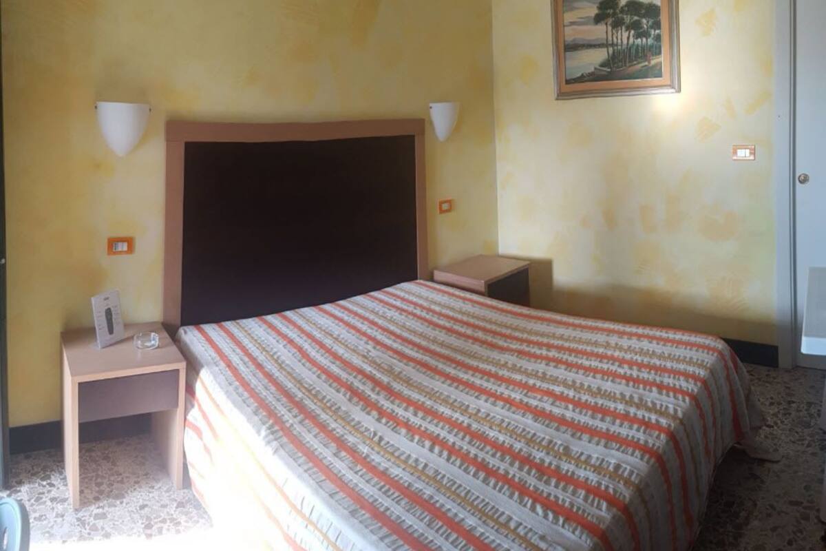A hotel room with a large bed, two bedside tables, a nightstand, a painting on the wall, and a door.