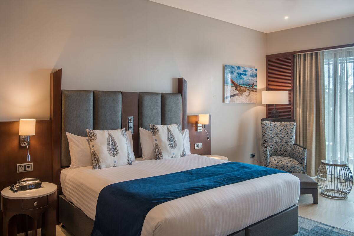 Ein Hotelzimmer mit einem großen Bett, zwei Nachttischen, einem Sessel und einem Bild an der Wand.