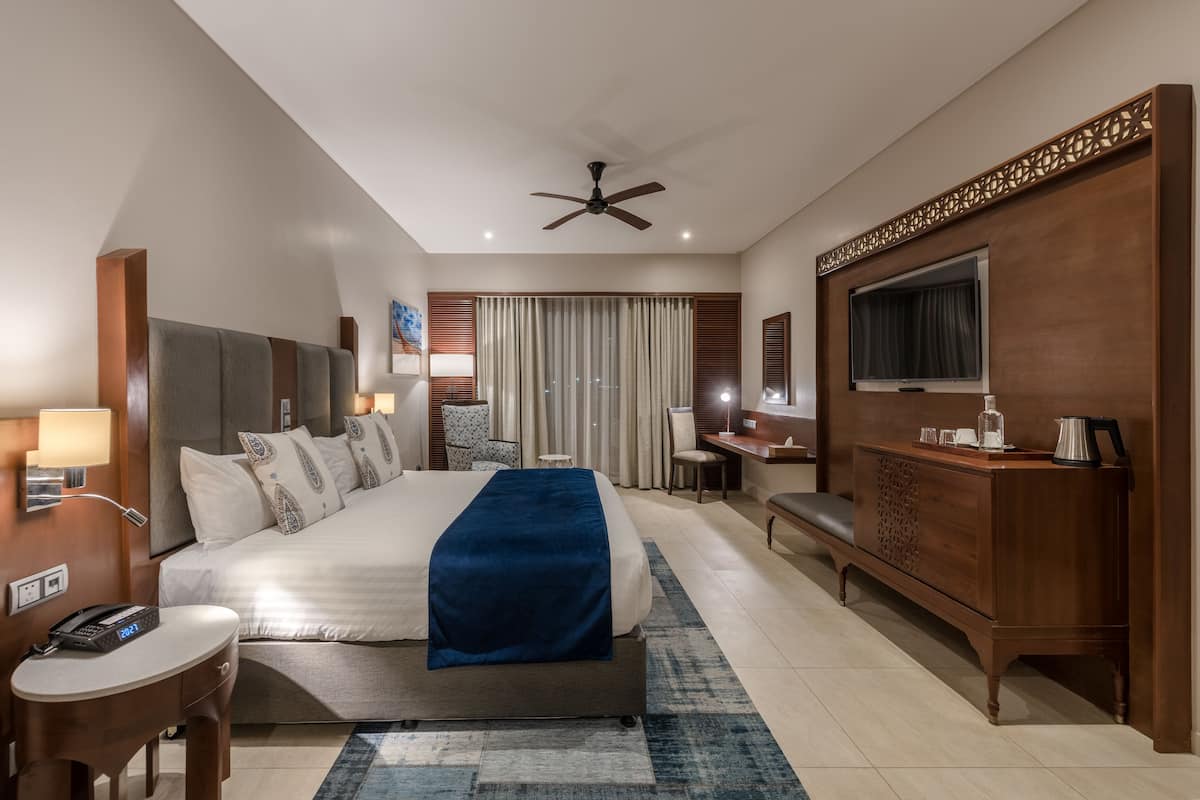 Ein Hotelzimmer mit einem großen Bett, einem Schreibtisch, einem Fernseher und einem Deckenventilator.
