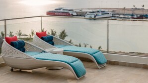 Dos sillones con cojines, una barandilla de cristal y vista al mar con barcos.