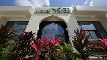 L'ingresso dell'Hotel Verde, dal design moderno, con ampie vetrate e piante tropicali circostanti.