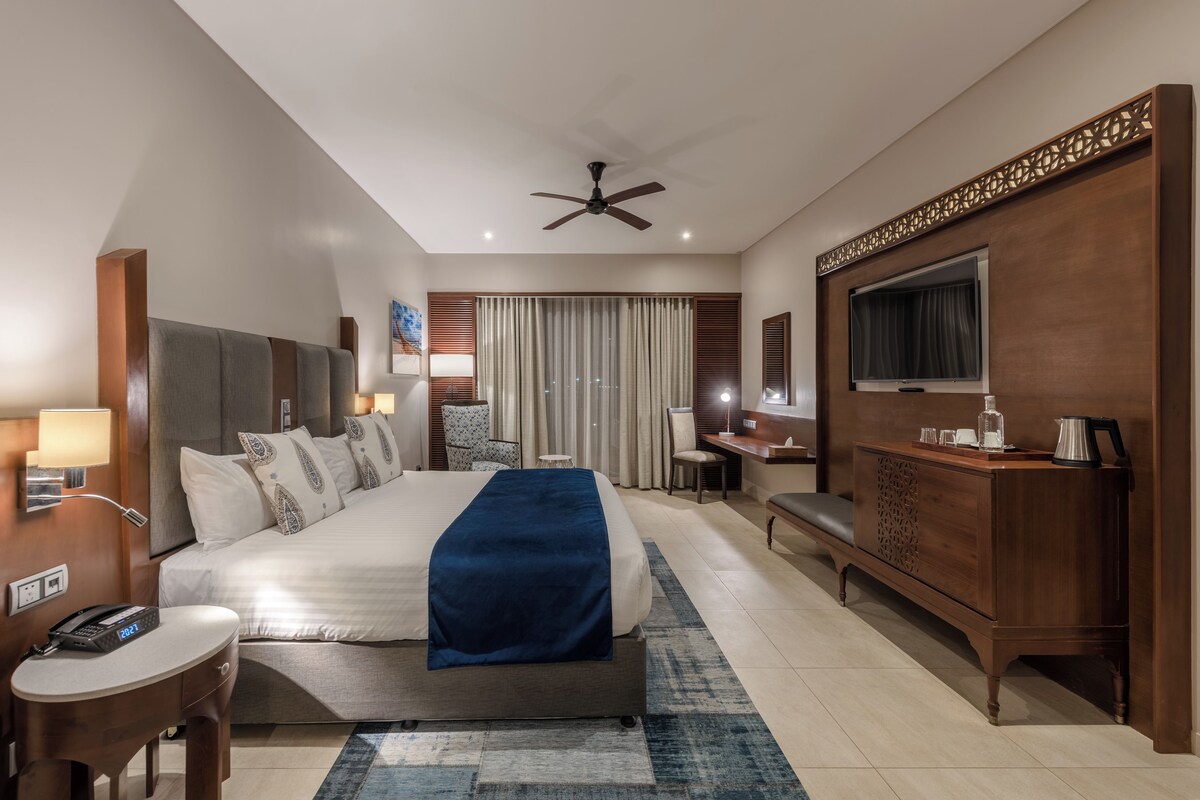 Une chambre d’hôtel moderne équipée d’un grand lit, d’un bureau, d’une télévision et d’un ventilateur de plafond.