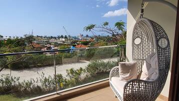 Un balcone con una sedia a dondolo in vimini, vista su una spiaggia e una città in lontananza.
