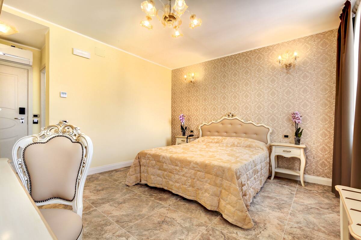 A bedroom with a large bed, a chair, a nightstand, and a chandelier.