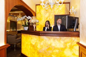 A reception desk with a marble wall, a potted orchid, and a chandelier.