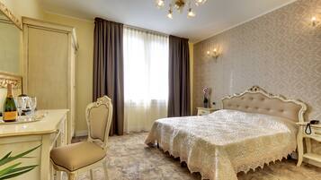 A bedroom with a large bed, a desk with a chair, a chandelier, and a window with curtains.
