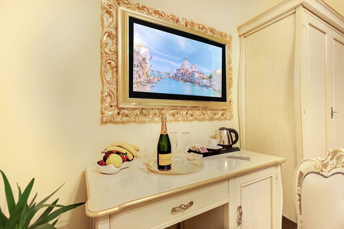 A hotel room with a television displaying a cityscape, a minibar, a white cabinet, and a decorative plant.