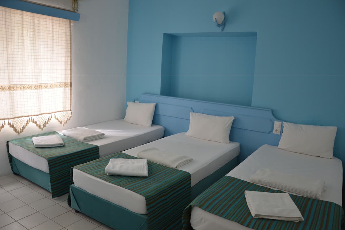 A hotel room with three single beds, each with a green-striped bedspread and white pillows.