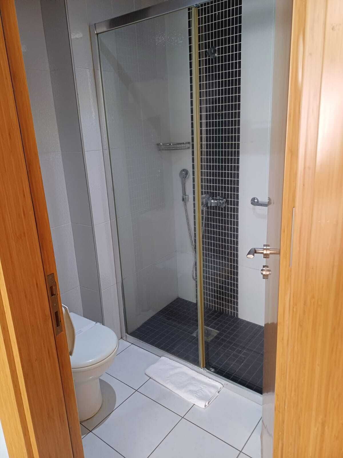 Un baño con ducha envuelta en vidrio, inodoro y piso de baldosas blancas.