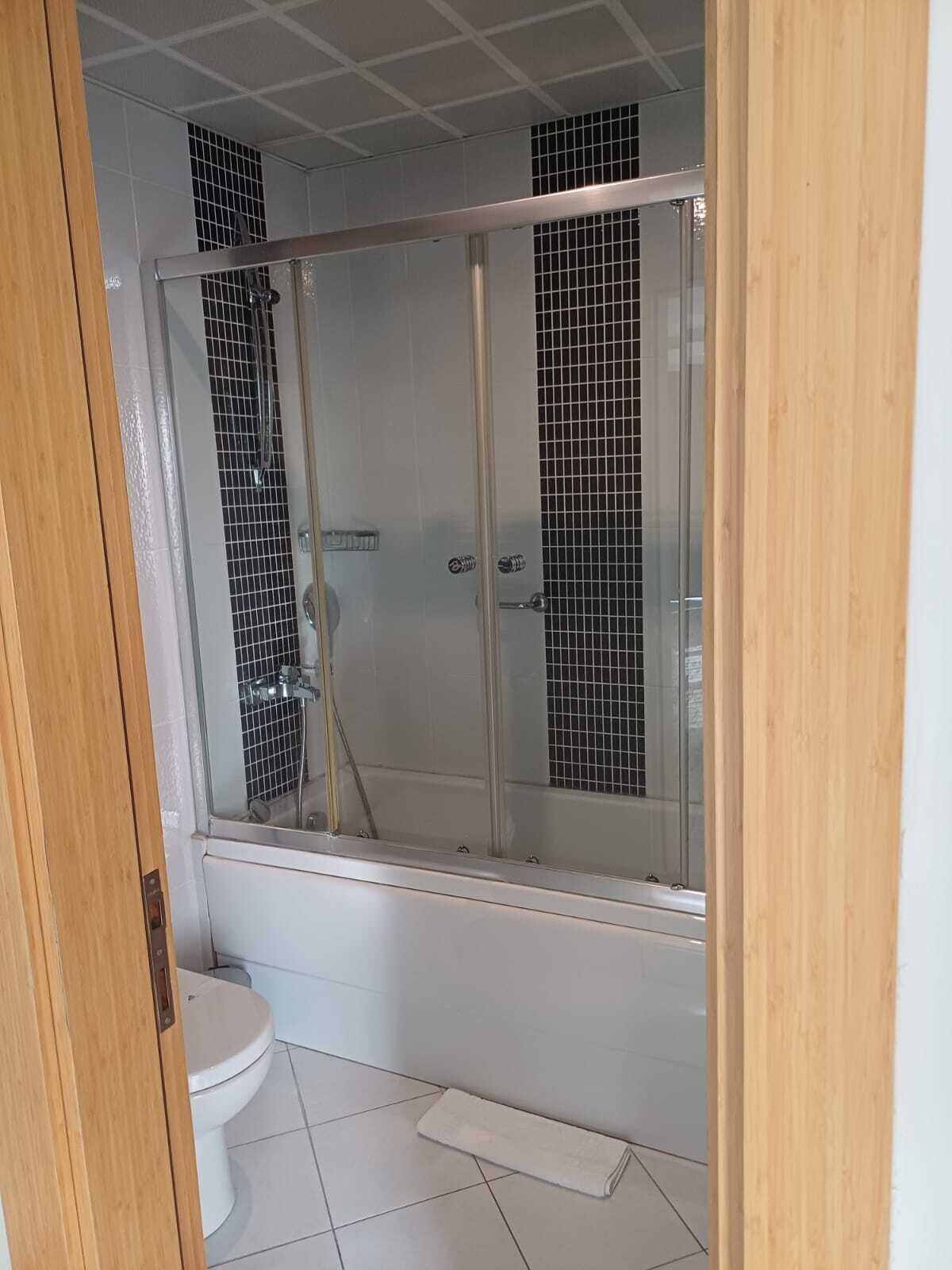 Une salle de bain avec une douche à parois de verre, des toilettes et une petite serviette sur le sol.