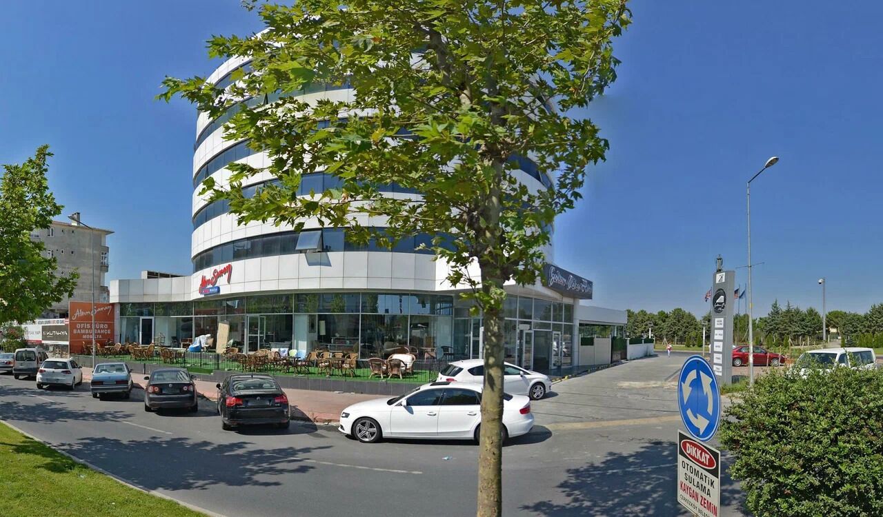 A modern building with a curved facade, a parking area with several cars, and a clear blue sky.