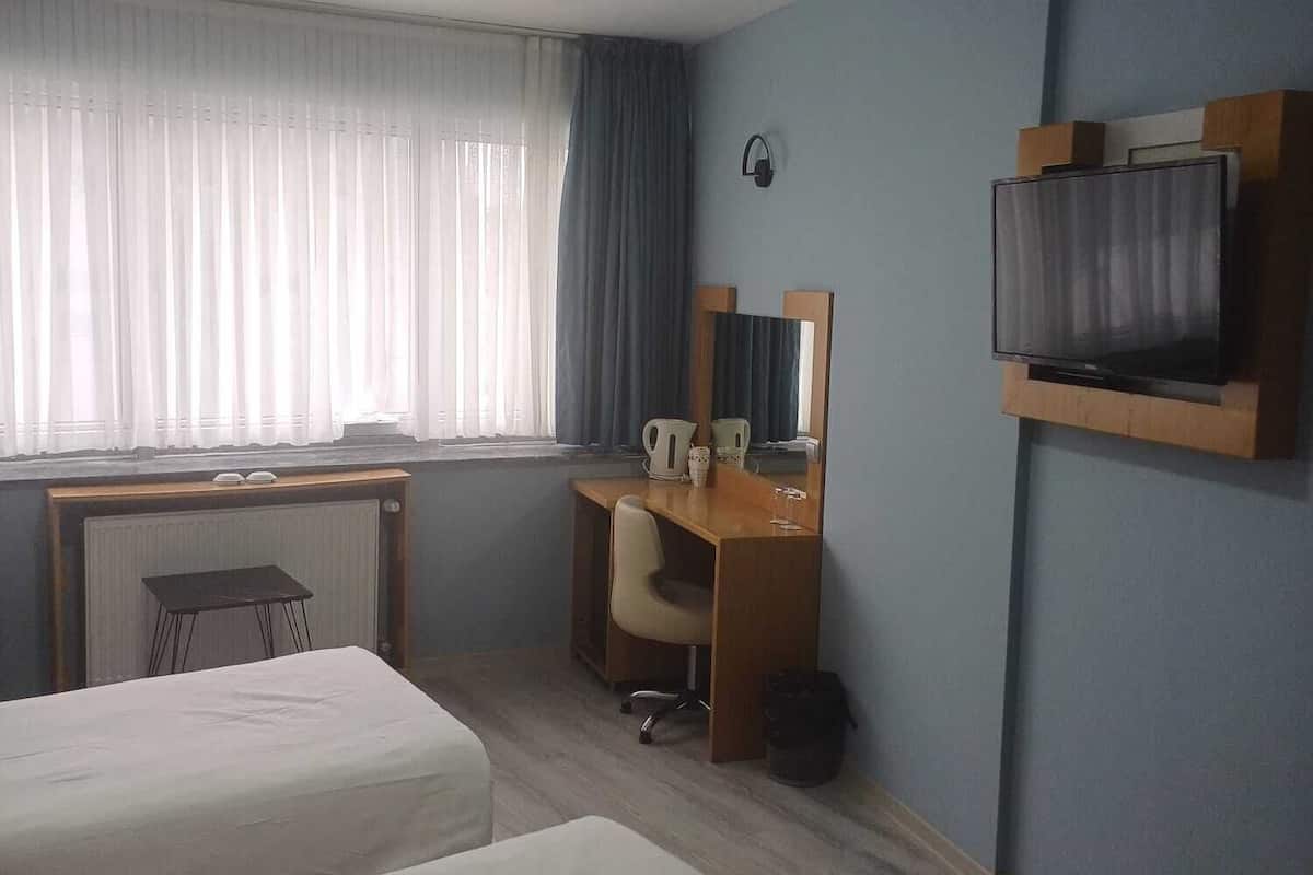 Ein Hotelzimmer mit zwei Betten, einem Schreibtisch mit Stuhl, einem Fernseher und einem Fenster mit Vorhängen.