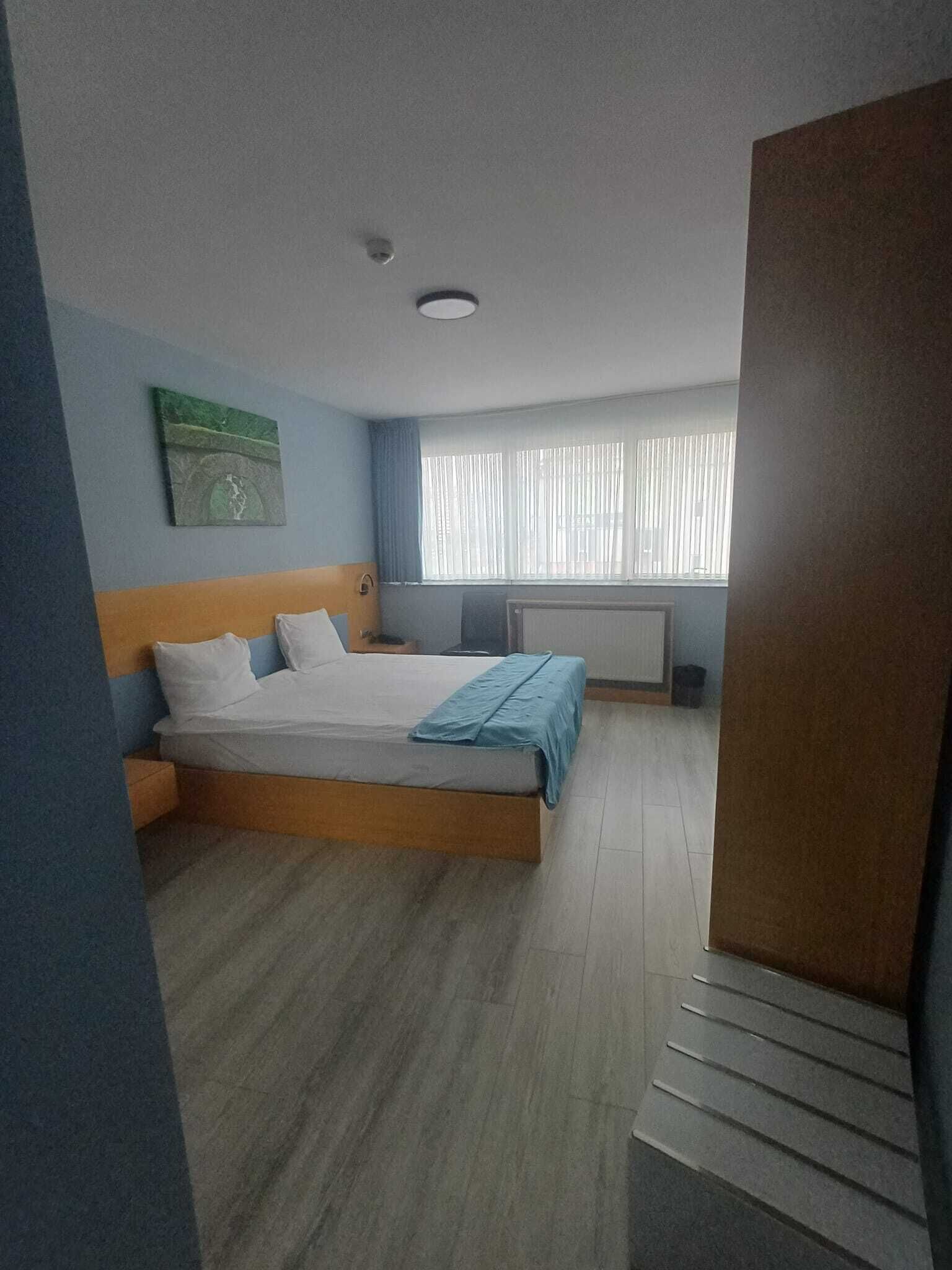 Ein Schlafzimmer mit Bett, einem Fenster mit Jalousien, einem Heizkörper und einem Wandbild.