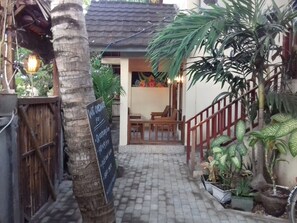 Step up to a charming outdoor dining area with a wooden staircase, table, and chairs, surrounded by lush greenery and a chalkboard sign.