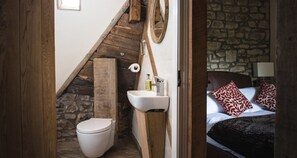 A compact bathroom with a wooden staircase, a toilet, a sink, and a bed with patterned pillows.
