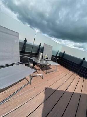 A deck with outdoor seating and a view of the ocean under a cloudy sky.