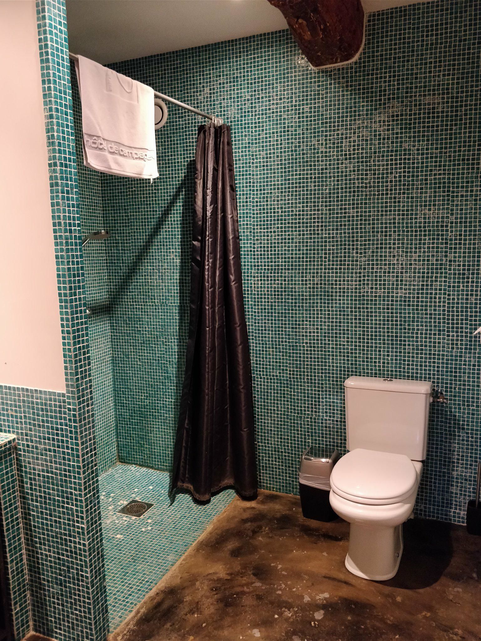 A bathroom with a toilet, a shower curtain, and a tiled wall.
