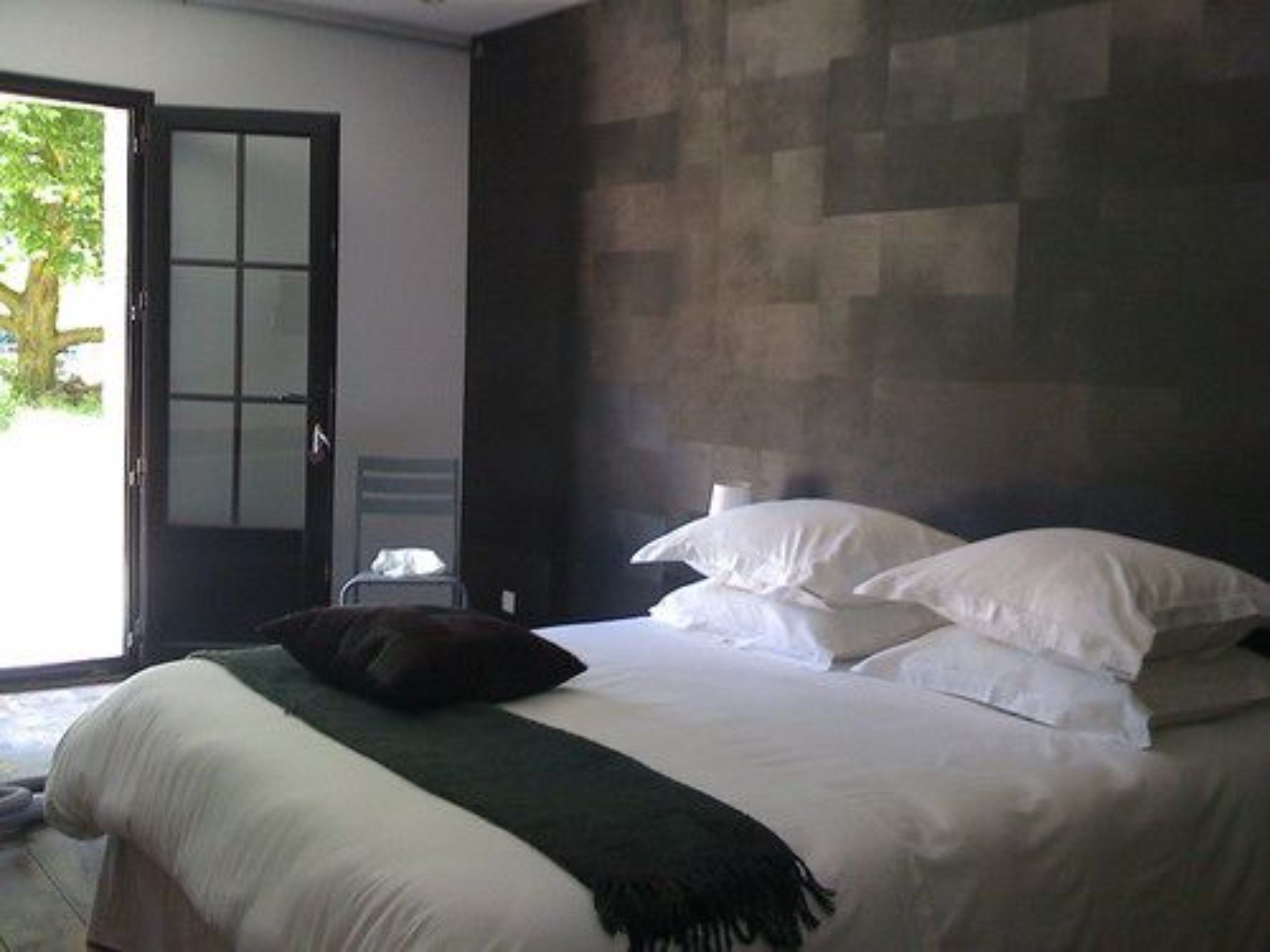 A bedroom with a bed, pillows, a blanket, a door, and a view of the outdoors.