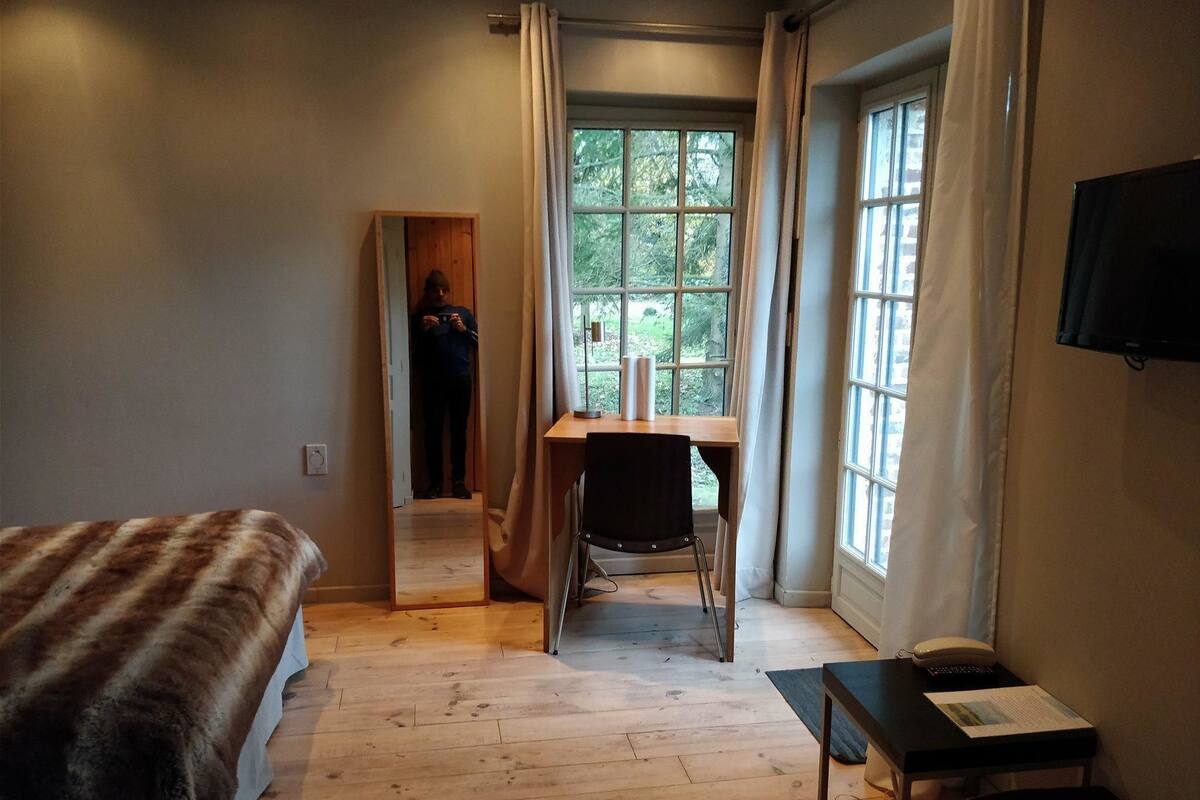 A bedroom with a bed, a desk, a chair, a TV, and a window with curtains.