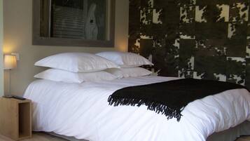 A bed with white linens, a black throw blanket, and a wooden nightstand with a remote control.