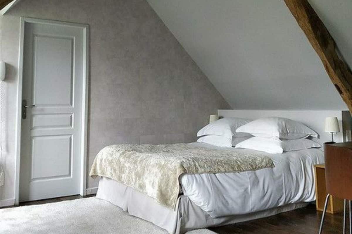 A bedroom with a sloped ceiling, a bed, a door, and a chair.
