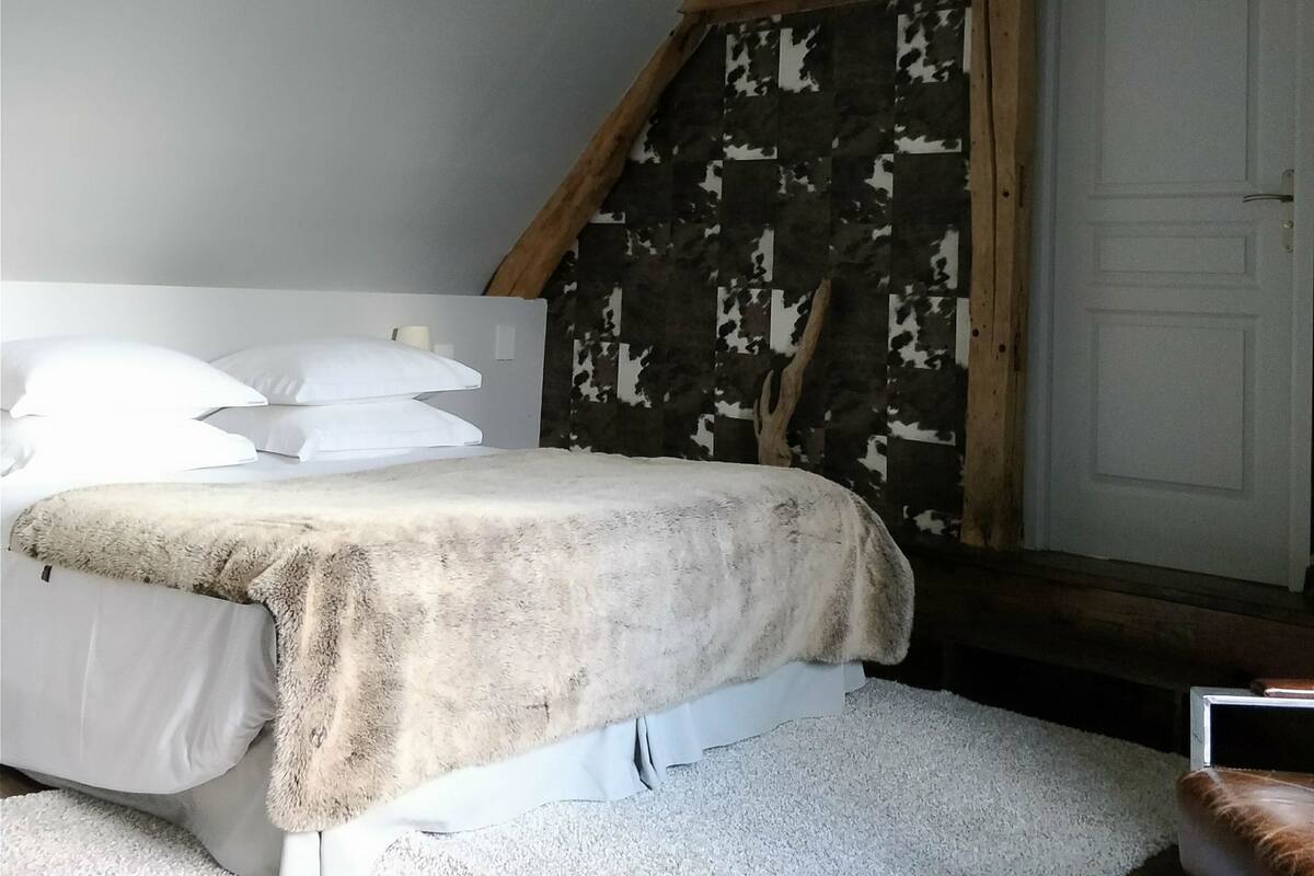 A bedroom with a sloped ceiling, a bed with white bedding, a wooden headboard, and a door with a simple design.