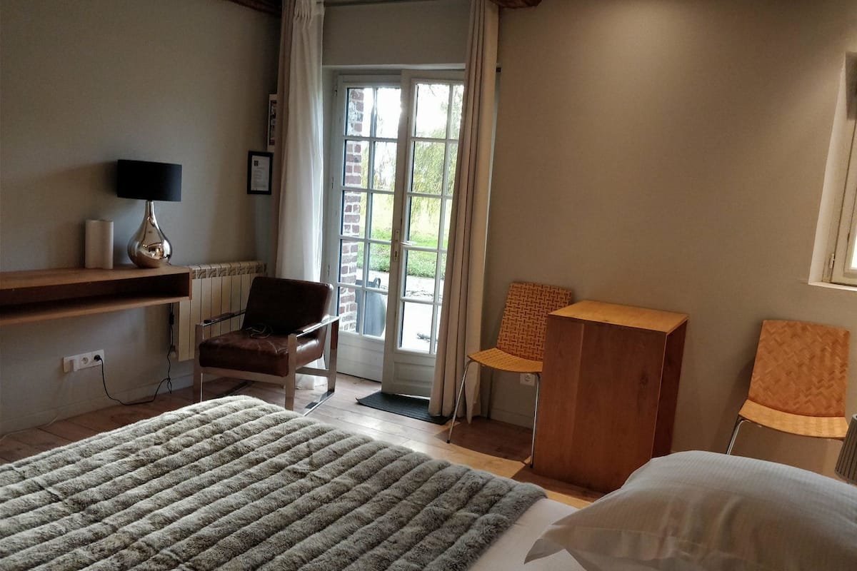 A bedroom with a bed, a chair, a desk, and a window with curtains.