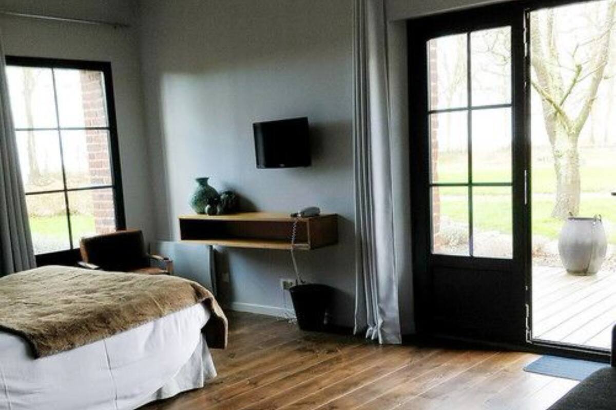 A bedroom with a bed, a television mounted on the wall, a window, and a door leading outside.
