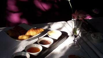 A table set with pastries, condiments, and a glass of water, with sunlight casting shadows.