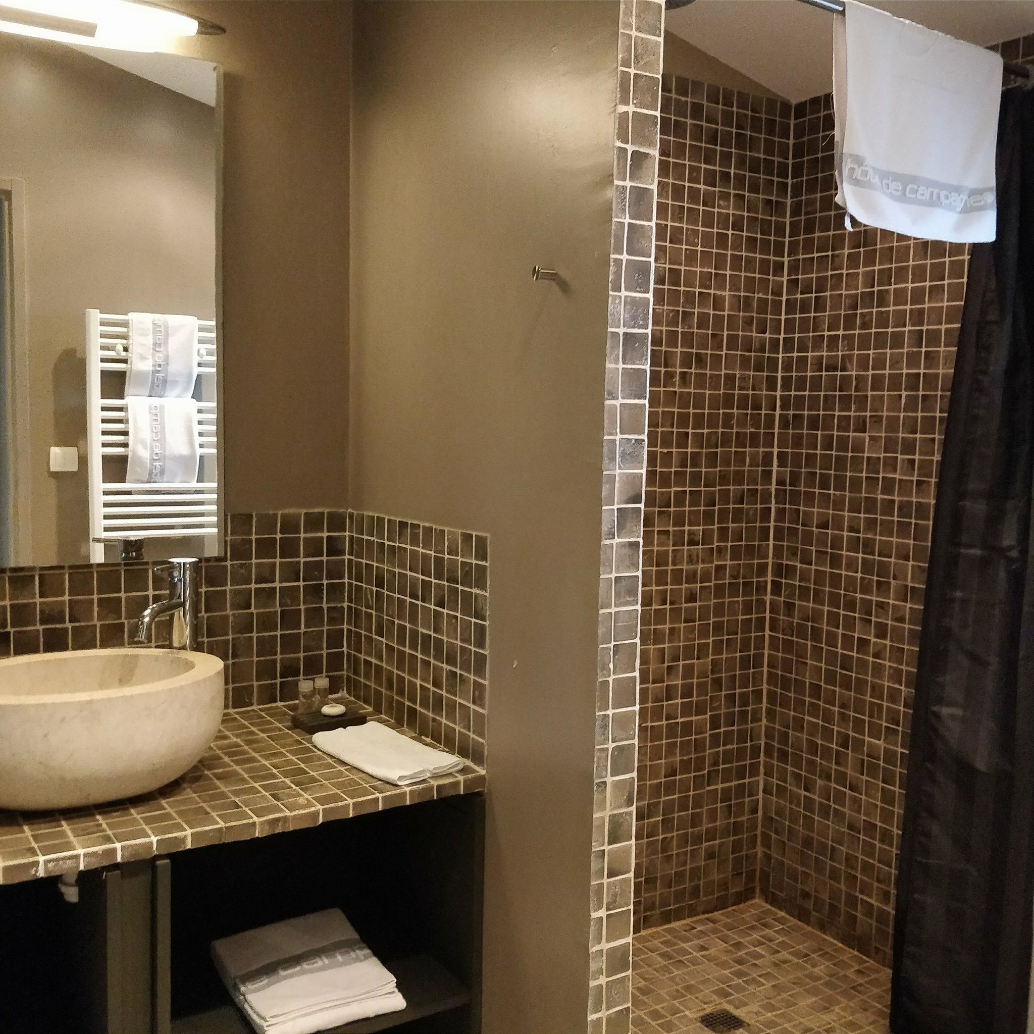 Un baño con un lavamanos grande, un espejo, un perchero para toallas y una zona de ducha con pared de azulejos.