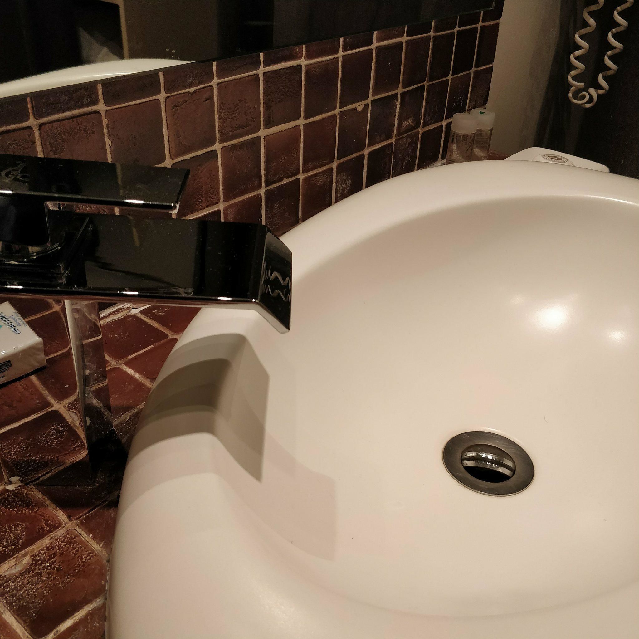 A white bathroom sink with a chrome faucet, a visible drain, and a tiled backsplash.
