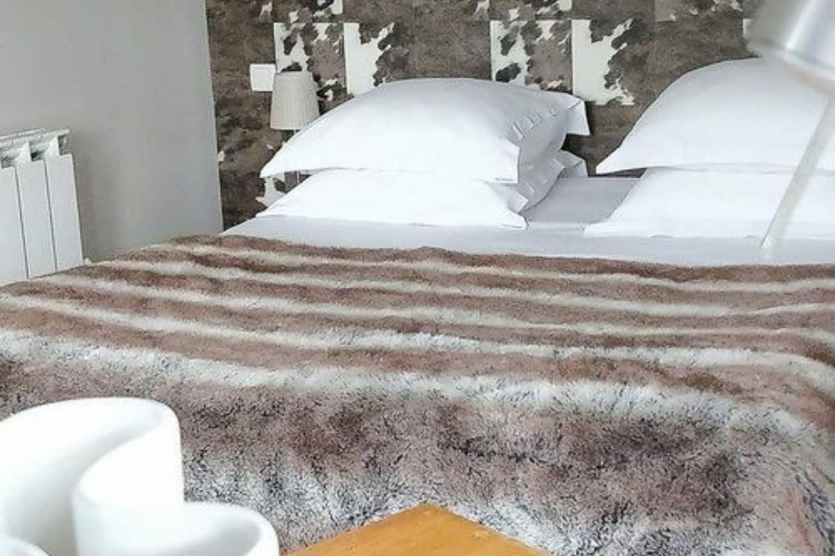 A hotel room with a bed, white pillows, a camouflage-patterned headboard, and a wooden side table.