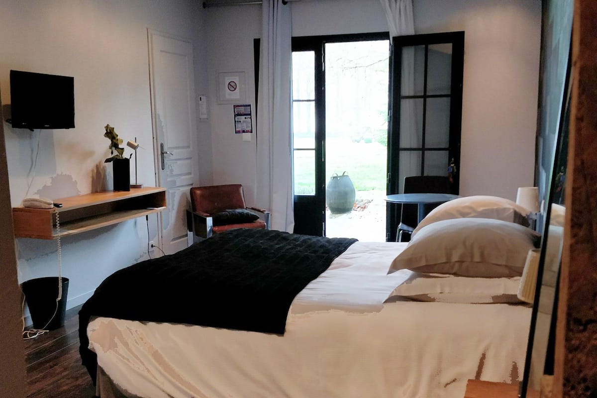 A bedroom with a bed, a chair, a table, a TV, and a window.