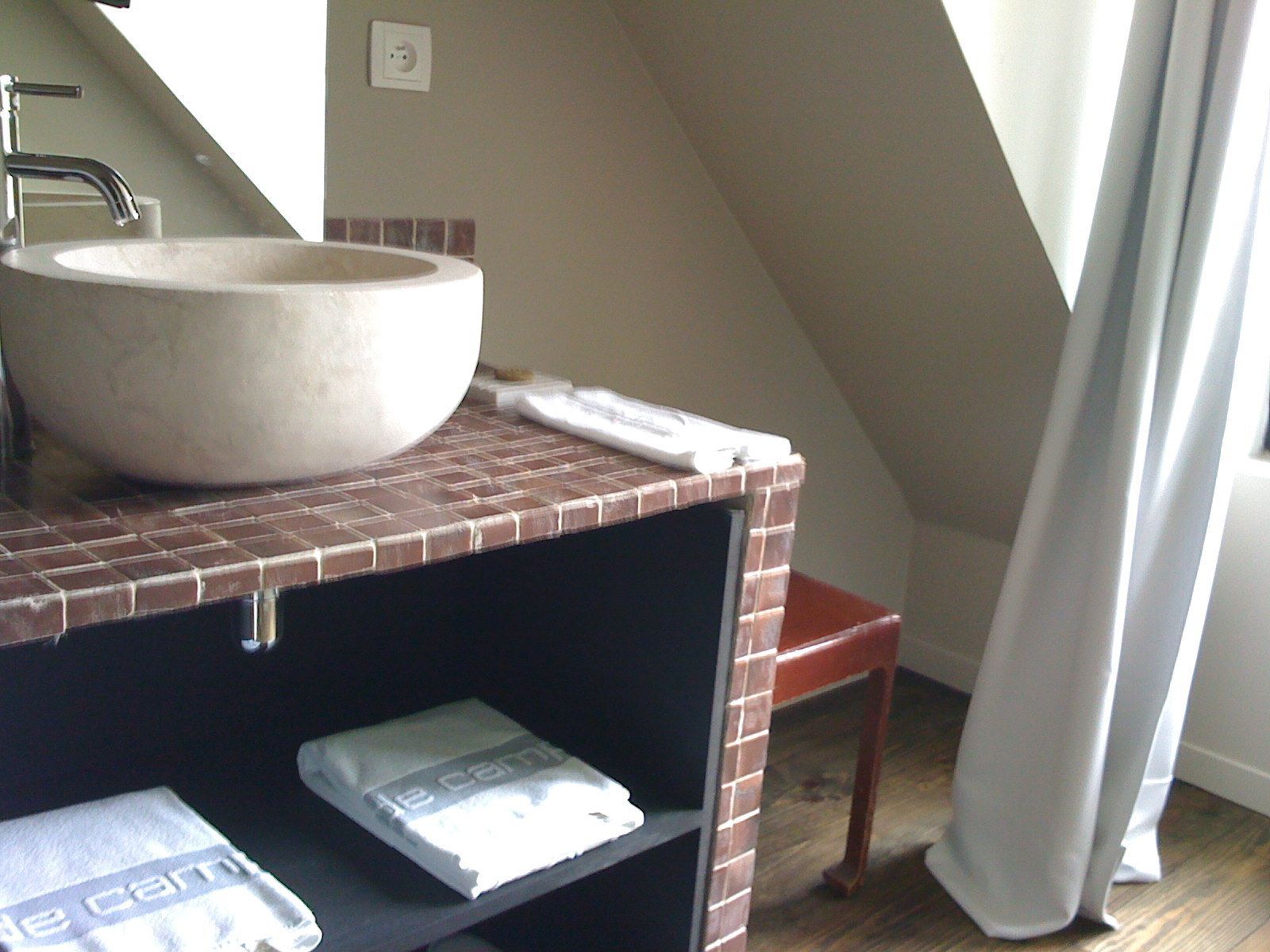 A bathroom with a large vessel sink, a towel rack, and a shelf with a towel.