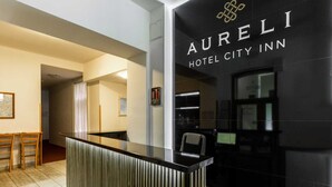 Een receptiebalie van een hotel met een modern design, een bord met 'Aureli Hotel City Inn' en een blik op het interieur, inclusief een ontvangstruimte en een gang.