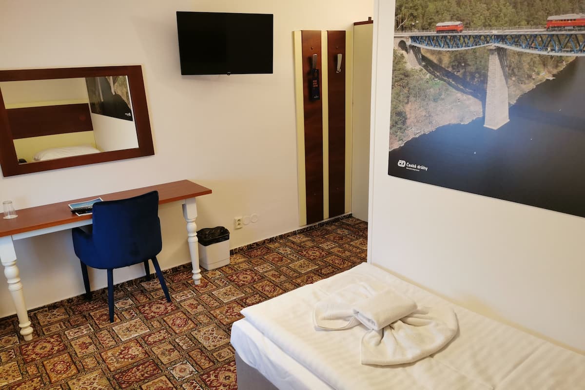 A hotel room with a bed, a desk with a chair, a television on the wall, and a patterned carpet.