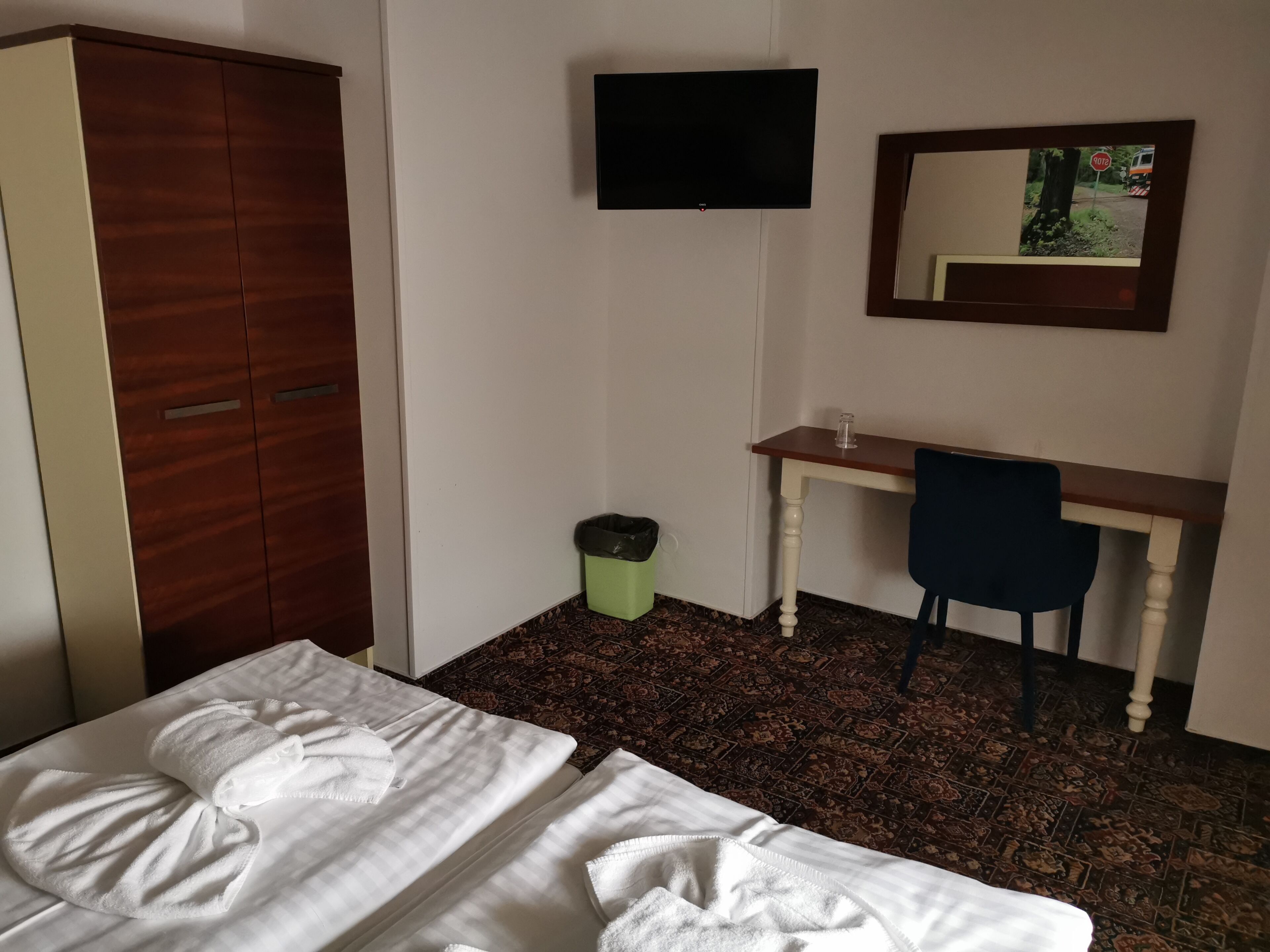 Hotelkamer met een bed, een bureau, een stoel, een kledingkast, een prullenbak en een aan de muur bevestigde televisie.