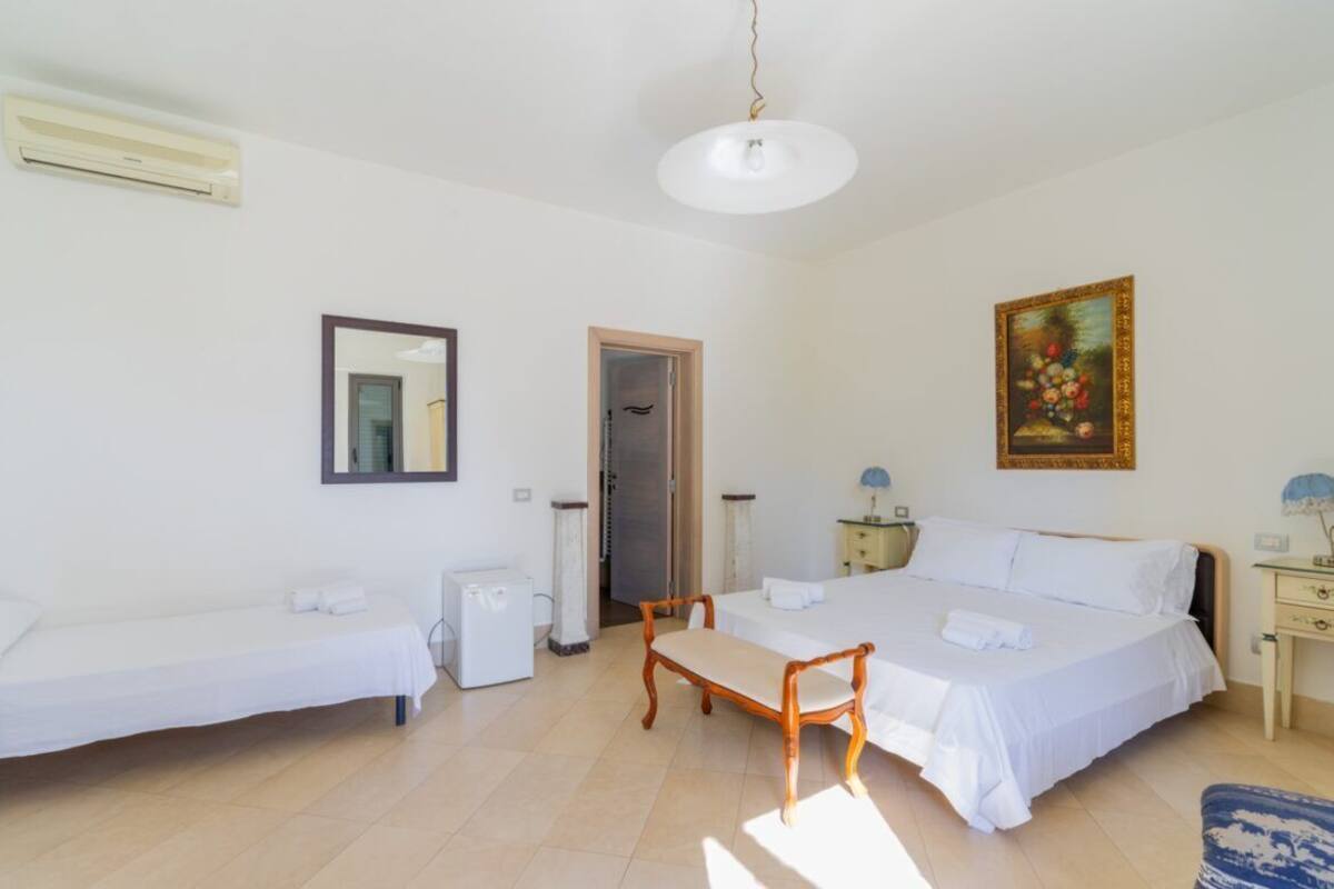 Ένα υπνοδωμάτιο με ένα κρεβάτι, ένα παγκάκι, ένα κομοδίνο, ένα φωτιστικό και έναν πίνακα στον τοίχο.