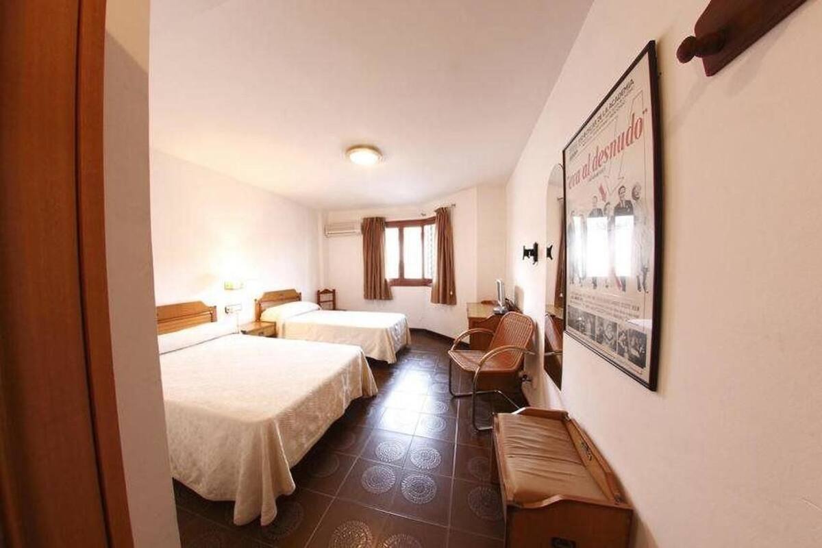 A hotel room with two beds, a desk, a chair, and a poster on the wall.