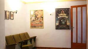 Un vestíbulo con una fila de sillas verdes, dos cuadros enmarcados en la pared y un cartel de cine.