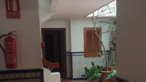 Un pasillo con baldosas estampadas, un extintor, una puerta de madera y plantas en macetas.